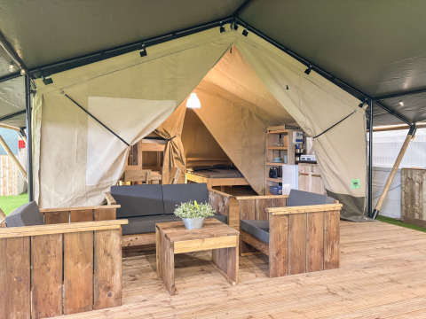 Intérieur d'une tente safari au Skovly Camping avec mobilier en bois et coin salon pour cinq personnes.