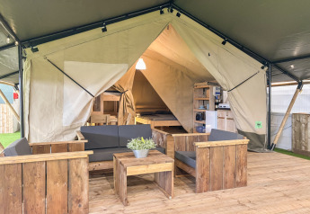 Interior de tienda safari en Skovly Camping con muebles de madera y área de estar para cinco personas.