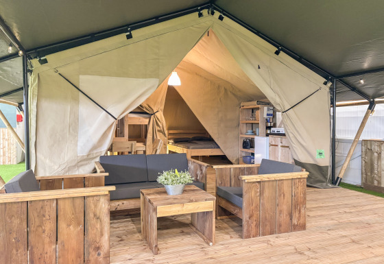 Innenansicht eines Safari-Zelts bei Skovly Camping, ausgestattet mit Holzmöbeln und Sitzecke für fünf.