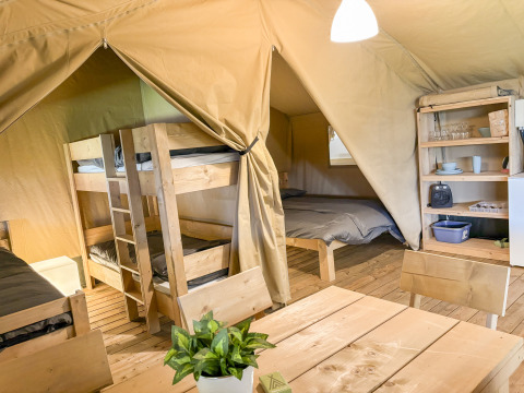 Indretning af en safaritelte med køjesenge, dobbeltseng, spisebord og åbne hylder på Skovly Camping.