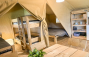 Interieur van een safaritent met stapelbedden, tweepersoonsbed, eettafel en planken bij Skovly Camping, Denemarken.