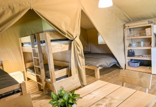 Intérieur d’une tente safari avec lits superposés, lit double, table à manger et étagères à Skovly Camping.