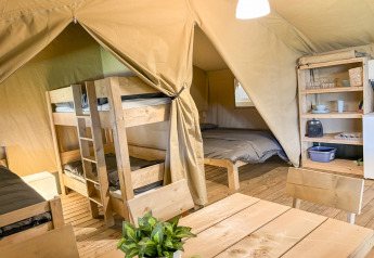 Intérieur d’une tente safari avec lits superposés, lit double, table à manger et étagères à Skovly Camping.