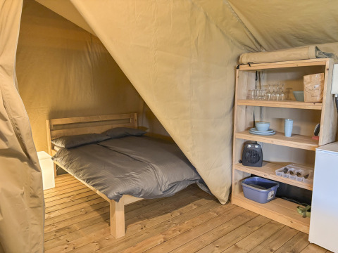 Indvendigt billede af en safaritelt med trægulv, dobbeltseng og reol med service på Skovly Camping.