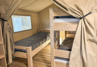 Intérieur d'une tente safari avec un lit simple, des lits superposés, sol en bois et rideaux beiges.