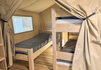 Innenaufnahme eines Safarizelts mit Einzelbett, Etagenbett, Holzboden und beigen Vorhängen.