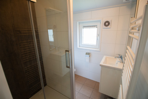 Bagno moderno con doccia in vetro, lavabo e finestra in uno chalet di lusso al Campeggio Mareveld, Paesi Bassi.