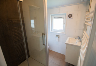 Bagno moderno con doccia in vetro, lavabo e finestra in uno chalet di lusso al Campeggio Mareveld, Paesi Bassi.