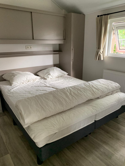 Camera da letto con due letti uniti, biancheria bianca, cuscini e finestra in un chalet nei Paesi Bassi.