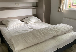 Bedroom with two single beds pushed together, white bedding, pillows, and a window at a Dutch lodge.