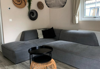 Stijlvolle woonkamer in Luxe chalet op Camping Mareveld in Nederland, met grijze hoekbank en decoratie.