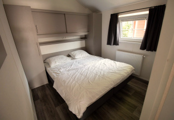 Modern slaapkamer in Luxe chalet op Camping Mareveld, Nederland, met groot bed en raam met gordijnen.