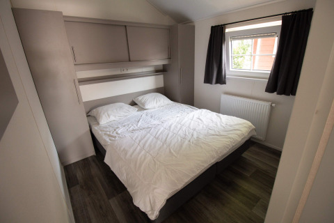 Modern bedroom at Luxe Chalet, Campsite Mareveld, Netherlands, featuring large double bed and window.