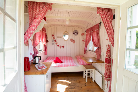 Interno accogliente della cabina Pipowagen al campeggio Mareveld nei Paesi Bassi con tende rosse e letto doppio.