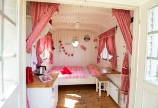 Cozy interior of the Pipowagen cabin at Campsite Mareveld, Netherlands, with red curtains and double bed.