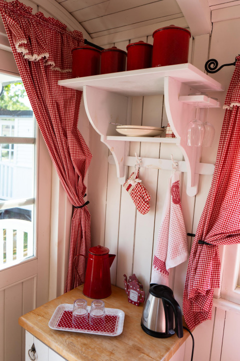 Angolo accogliente della cabina Pipowagen con tenda a quadretti rossa e utensili da cucina coordinati.