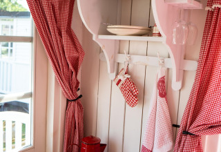 Cozy corner of Pipowagen cabin at Campsite Mareveld with red kitchenware, gingham curtains, and kettle.
