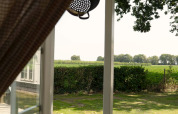 Uitzicht vanuit Pipowagen bij Campsite Mareveld in Nederland met open deur, gordijn en groene natuur.