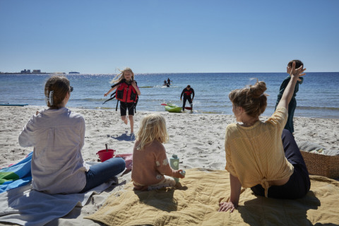 Gezinnen genieten van de zon op het strand bij Nordskoven Strand Camping; kinderen spelen en volwassenen ontspannen.