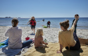 Familias disfrutan de un día soleado en la playa de Nordskoven Strand Camping, niños juegan y adultos descansan.