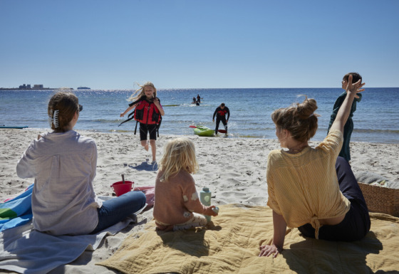 Gezinnen genieten van de zon op het strand bij Nordskoven Strand Camping; kinderen spelen en volwassenen ontspannen.