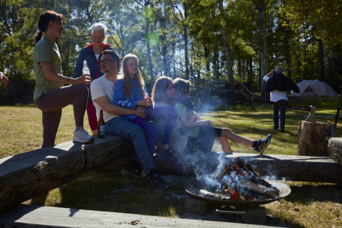 Familie en vrienden zitten bij een kampvuur op Nordskoven Strand Camping in Denemarken.