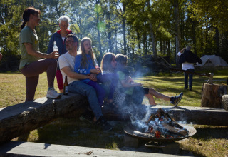 Familie en vrienden zitten bij een kampvuur op Nordskoven Strand Camping in Denemarken.