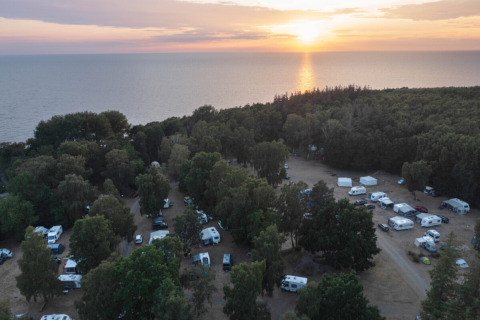 Luchtfoto van Nordskoven Strand Camping met campers en bomen aan zee bij een mooie zonsondergang.