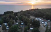 Vue aérienne de Nordskoven Strand Camping, caravanes et arbres près de la mer lors d’un superbe coucher de soleil.