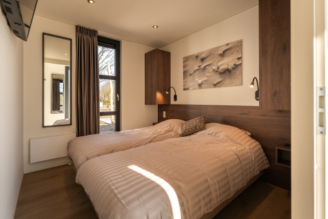 Moderne slaapkamer met twee eenpersoonsbedden, houten accenten, raam en wandkunst in Villa Bloomingdale.