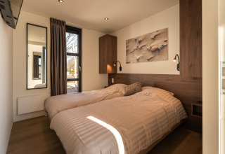 Moderne slaapkamer met twee eenpersoonsbedden, houten accenten, raam en wandkunst in Villa Bloomingdale.