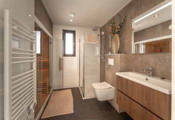 Modernes Badezimmer mit Holzschränken, Glasdusche, Sauna, Handtuchheizung und großer Vase.