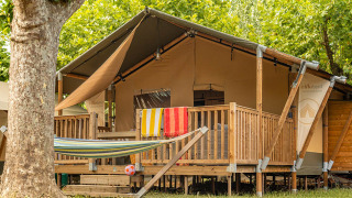 Tenda safari Villatent Outback con veranda in legno, amaca e asciugamani colorati stesi fuori.