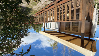 Buitenfoto van een huisje genaamd Cottage met airconditioning, houten terras en zonnescherm onder blauwe lucht.