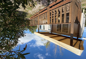 Outdoor photo of a cabin named Cottage with air conditioning, wooden deck, and awning under blue sky.