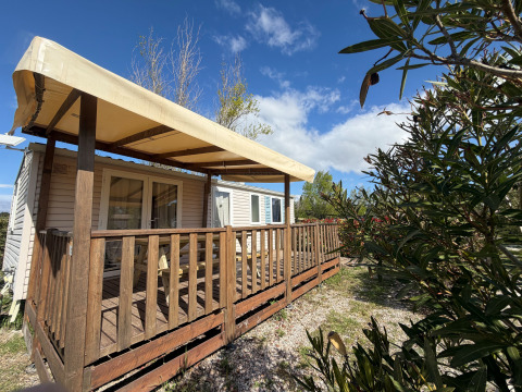 Foto all'aperto di una casetta chiamata Cottage con aria condizionata, veranda in legno e tenda sotto cielo blu.