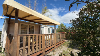 Foto all'aperto di una casetta chiamata Cottage con aria condizionata, veranda in legno e tenda sotto cielo blu.