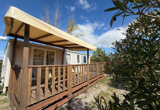 Buitenfoto van een huisje genaamd Cottage met airconditioning, houten terras en zonnescherm onder blauwe lucht.