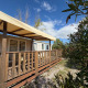 Buitenfoto van een huisje genaamd Cottage met airconditioning, houten terras en zonnescherm onder blauwe lucht.