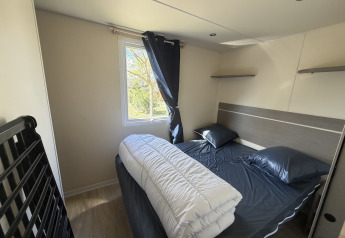 Bedroom at the Cottage in Campsite Seasonova Ensoya, France, featuring a double bed, window and dark bedding.