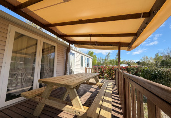 Wooden terrace with bench table and awning at Cottage in Campsite Seasonova Ensoya, France, on a sunny day.