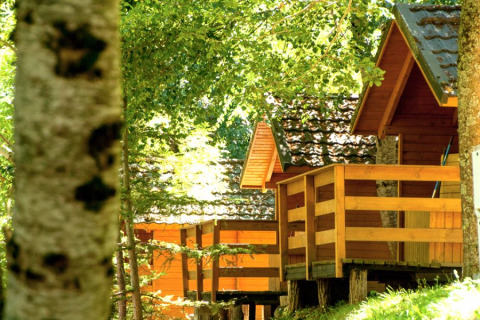 Wooden cabins with porches surrounded by green trees at Bedura Park Campsite, Spain, in sunlight.