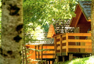 Bungalows de madera con terrazas rodeados de árboles verdes en Camping Bedura Park, España, soleado.