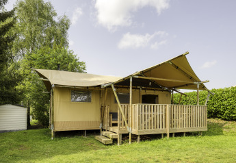Safari-Zelt Dreamer mit Holzveranda, auf einer Wiese gelegen und von Bäumen und Hecken umgeben.