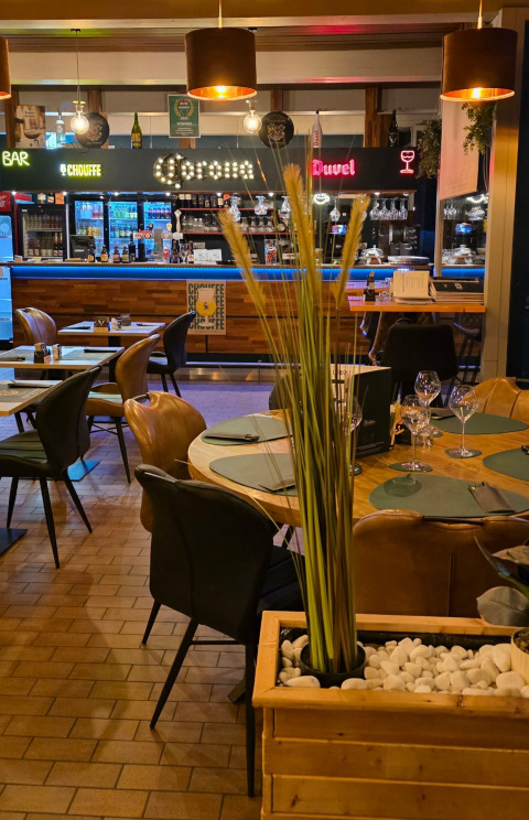 Binnenrestaurant bij een glamping, met gedekte tafels, decoratieve plant en moderne bar op de achtergrond.