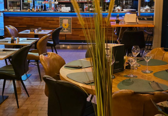 Restaurant intérieur de glamping, tables dressées, plante décorative et bar moderne éclairé en arrière-plan.