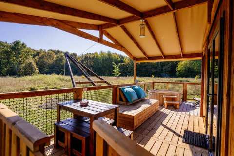 Holzveranda der Océania Lodge im Domaine EcÔtelia, Frankreich, mit Sitzplätzen und Blick auf Wiese und Wald.