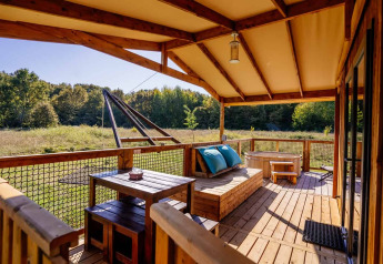 Wooden terrace at Océania Lodge, Domaine EcÔtelia, France, with rustic furniture and scenic field and forest views.