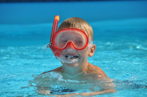 Dreng med rødt snorkeludstyr svømmer i poolen hos Skovly Camping, feriepark i Region Sjælland, Danmark.