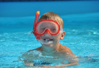 Dreng med rødt snorkeludstyr svømmer i poolen hos Skovly Camping, feriepark i Region Sjælland, Danmark.